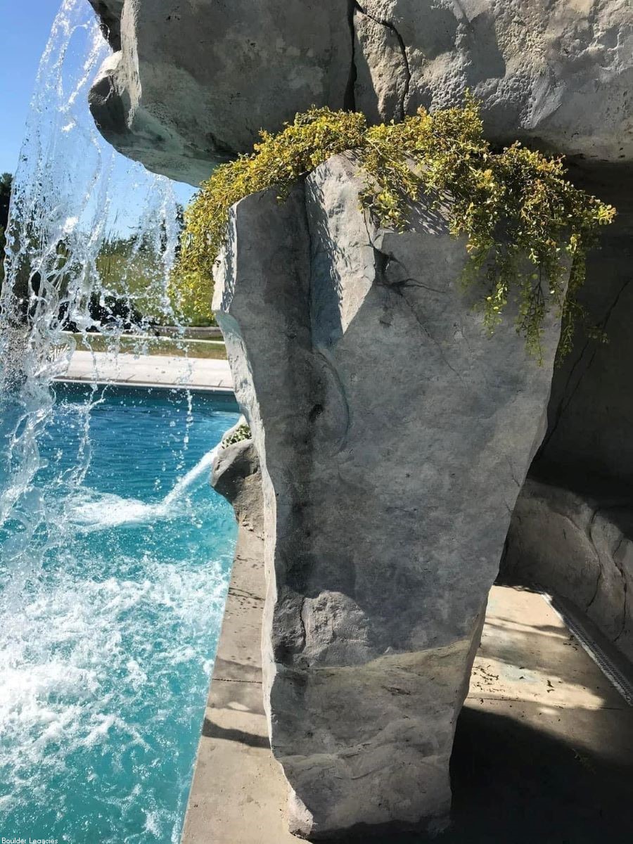 Picutre showing a rockwaterfall for a swimming pool. You can see a tall custom made waterfall splashing water into a swimming pool.