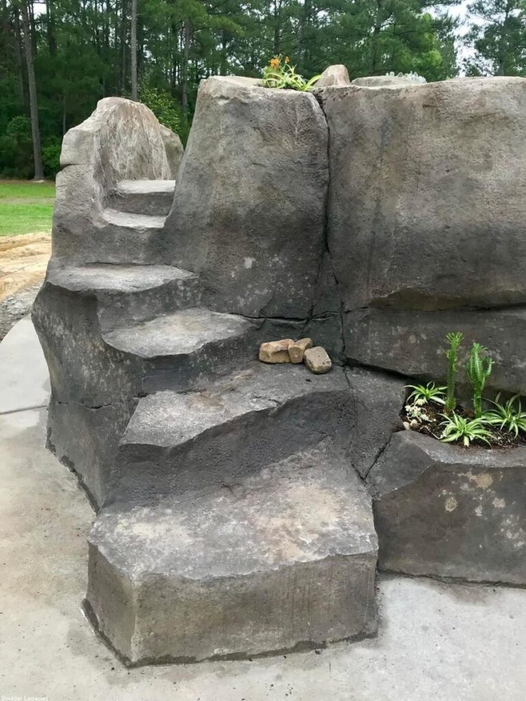 Image of the back of a rock waterfall. You can see rock steps leading to the top of the pool waterfall.