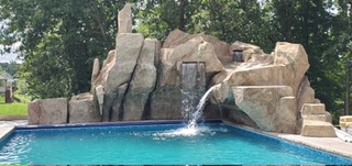 Custom faux rock waterfall grotto and waterslide feature built onto a residential swimming pool by Boulder Legacies